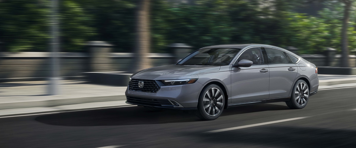 3/4 front view of grey Accord driving on upper-class city street lined with trees.