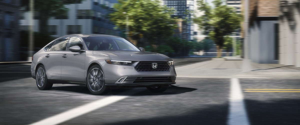 3/4 front view of grey Accord making a turn on a city street.