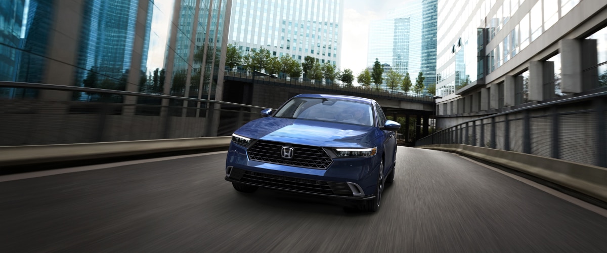 Front view of blue Accord driving toward camera on an empty city street amid buildings.