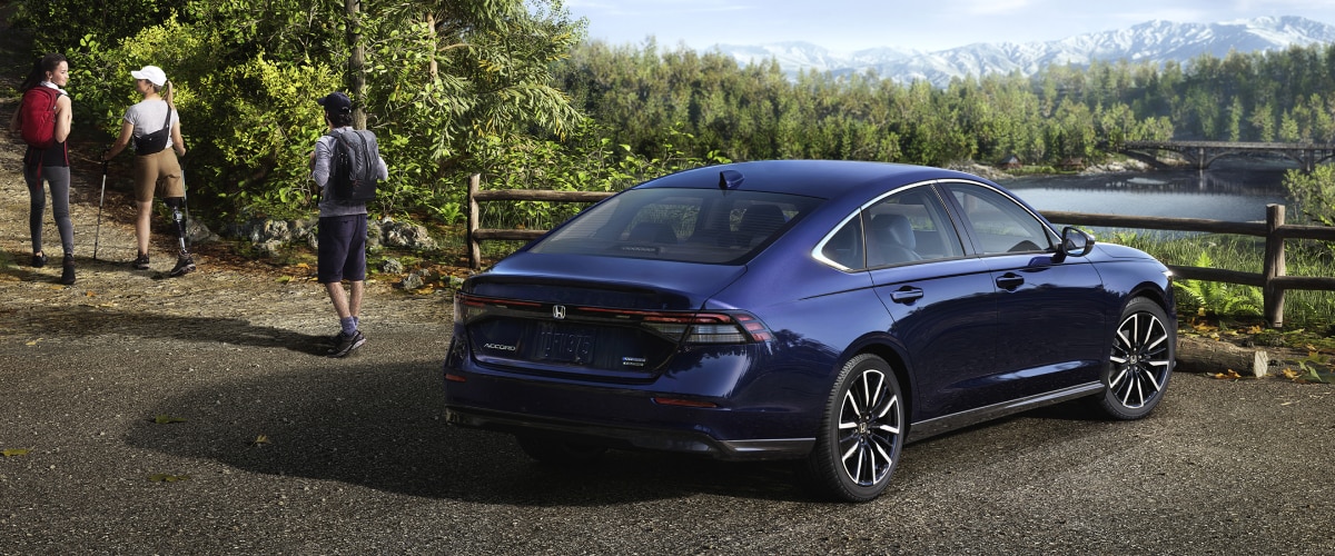 3/4 rear view of a parked blue Accord overseeing a forest and mountains. A hiker walking away from it.