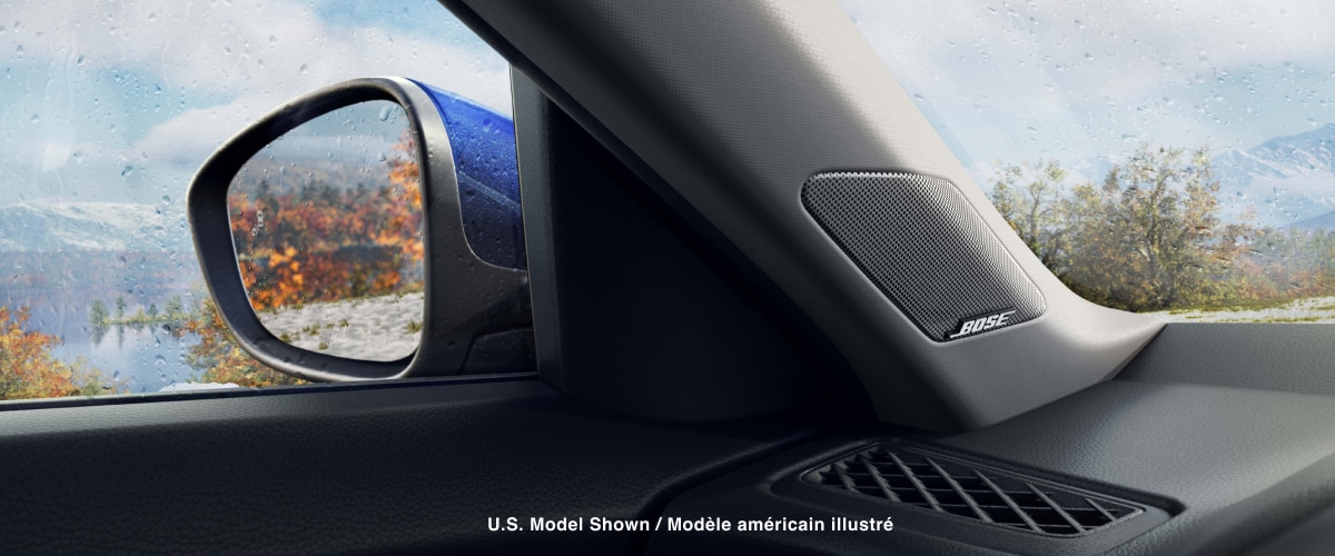 Interior view of door mirror and BOSE® speaker. Out the driver-side window: a mountain range, lake, and trees with orange leaves.