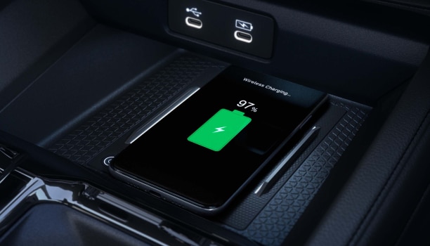 Gros plan d’un téléphone intelligent compatible qui se recharge sans fil sur le tapis de recharge devant le levier de vitesses.