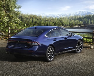 3/4 rear view of a parked blue Accord overseeing a forest and mountains. A hiker walking away from it.