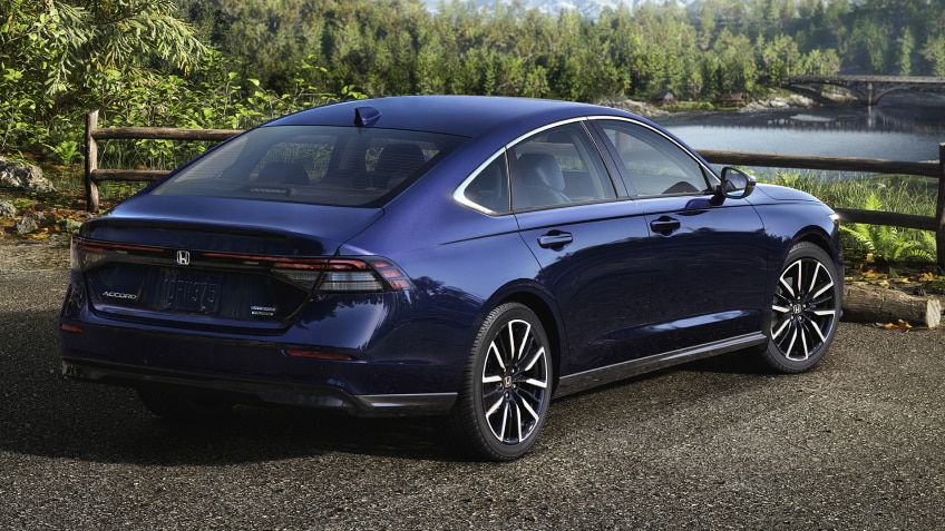 3/4 rear view of a parked blue Accord overseeing a forest and mountains. A hiker walking away from it.