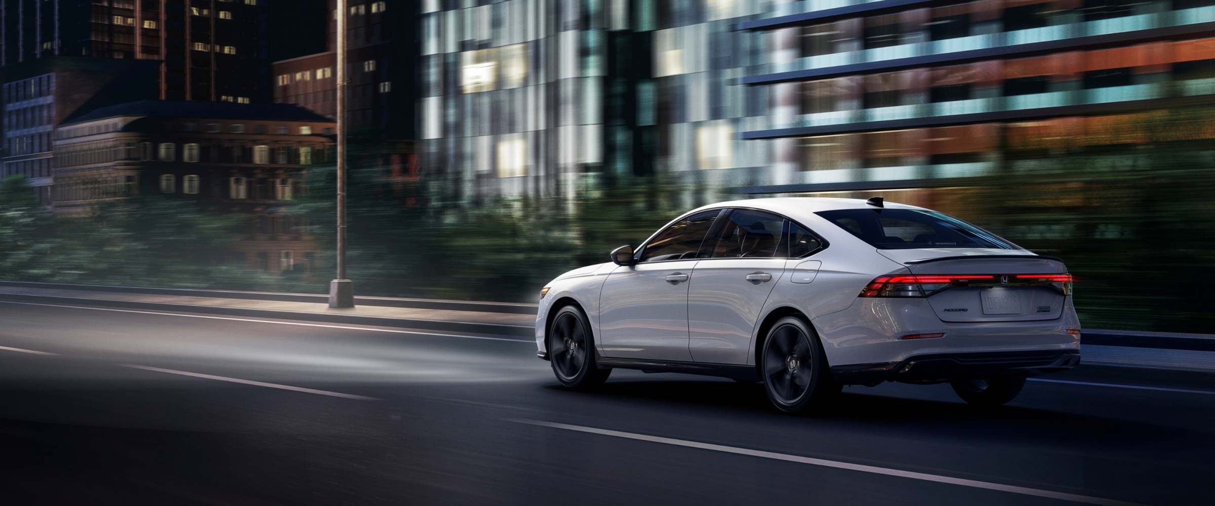 3/4 rear view of a white Accord driving on a city street.