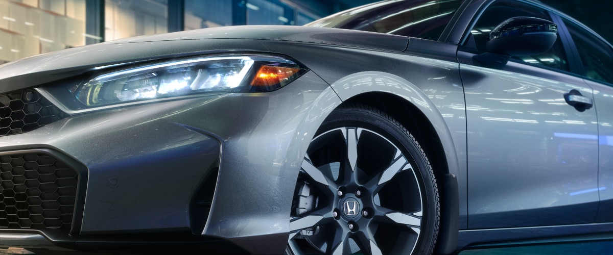 Close up of front view of a grey hatchback with lights on.