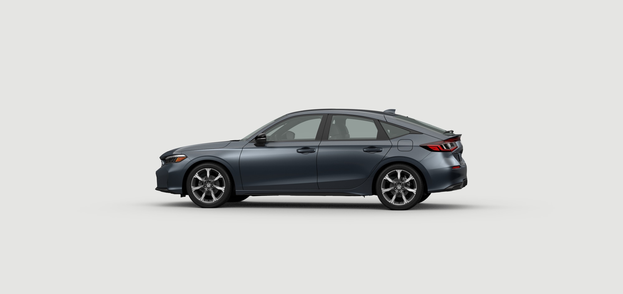 Side driver-side view of 2025 Civic Hatchback Sport Touring Hybrid in Meteoroid Grey Metallic colour on white space.