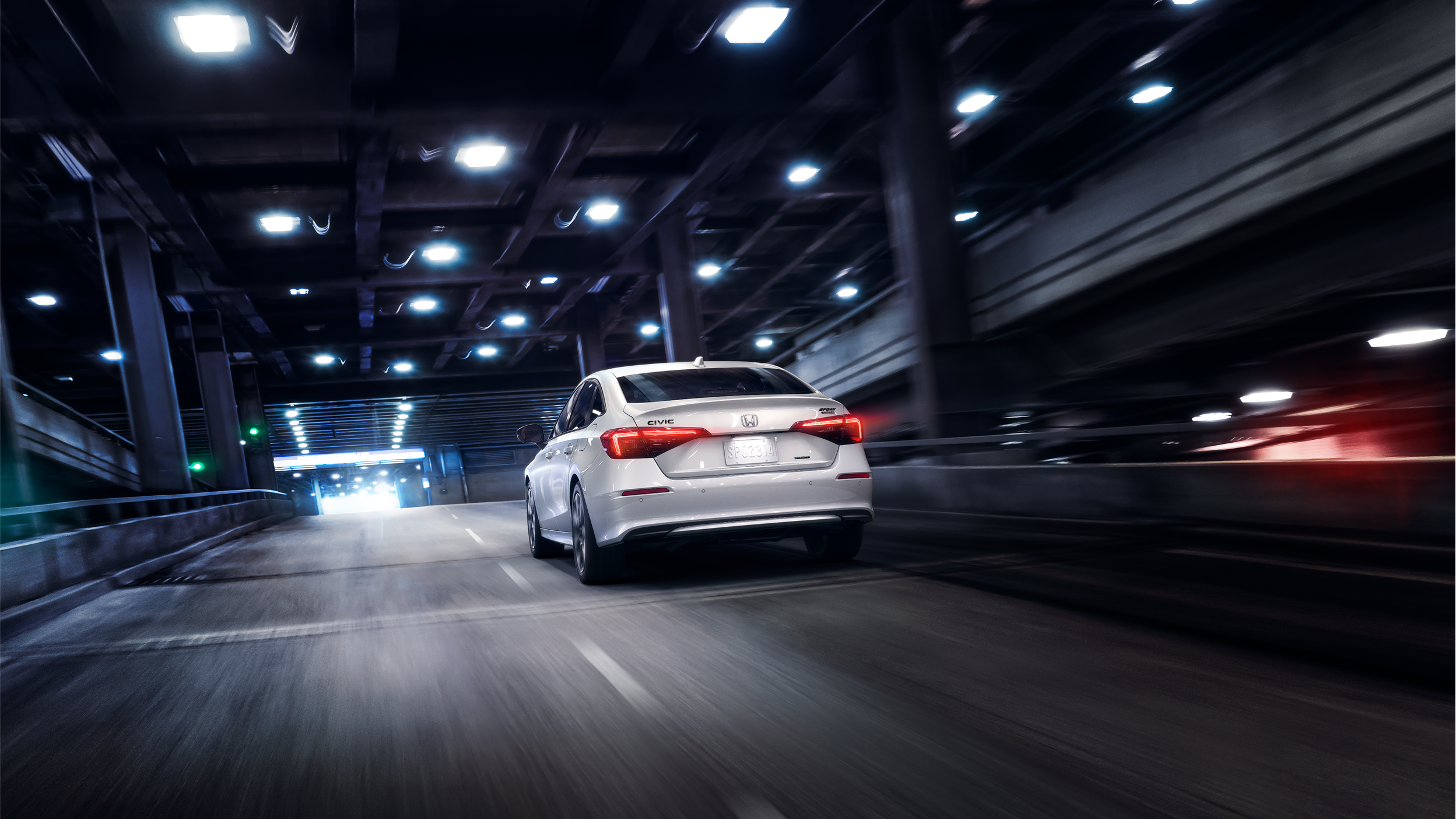 3/4 rear wide view of a black Civic Sedan driving by upscale boutique architecture on a city street during the day.