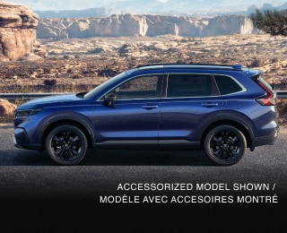 3/4 front view of grey CR-V, with two bikes on the roof racks, driving on a winding desert canyon highway. 