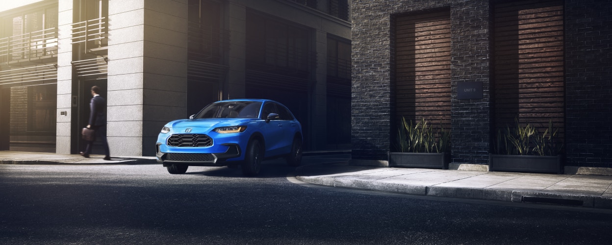 3/4 front view of blue HR-V pulling out of an alleyway in the city.