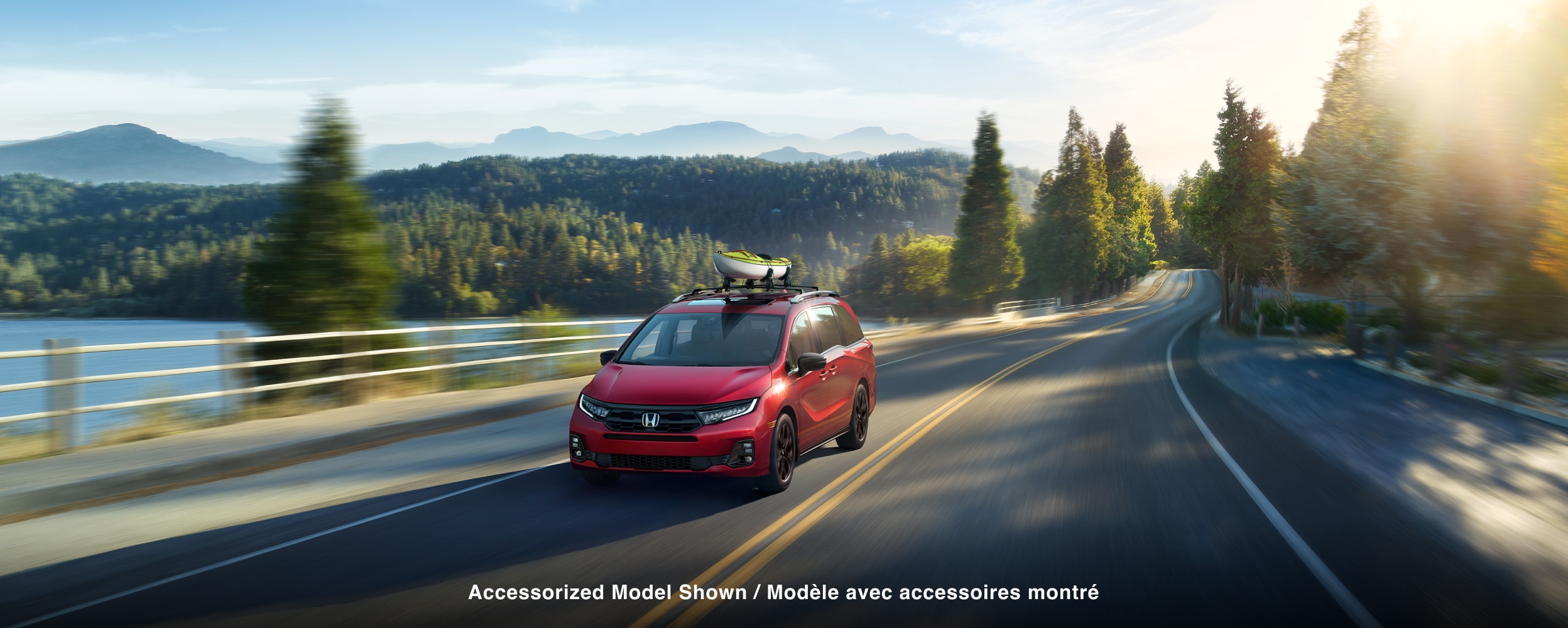 3/4 front view of red Odyssey driving on lakeside road.