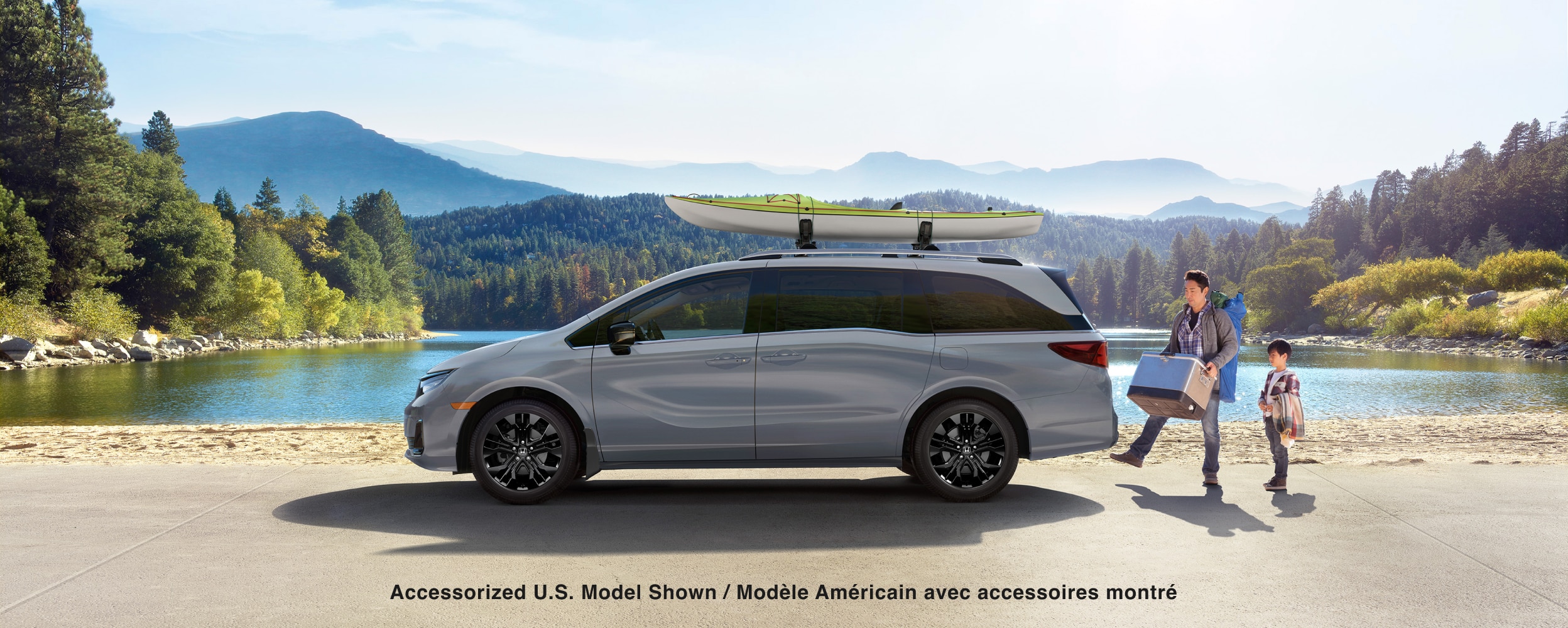 Vue latérale d’une Odyssey blanche stationnée au bord d’un lac. Un père et son enfant chargent l’espace de chargement.