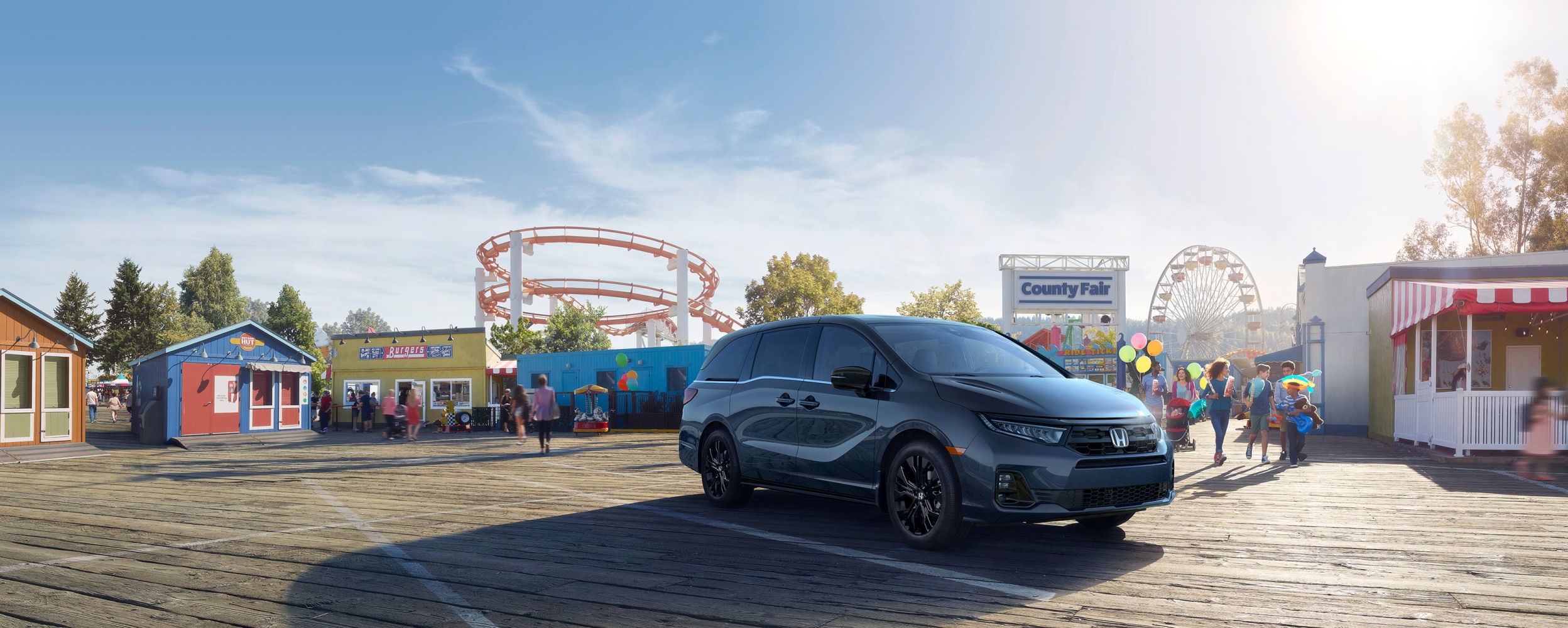 3/4 side front view of grey Odyssey parked in front of a county fair with roller coaster and ferris wheel int he background.