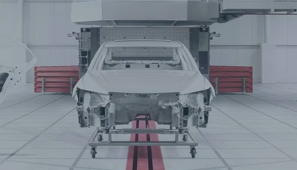 The frame of a Honda vehicle is on a lift inside an white industrial space.