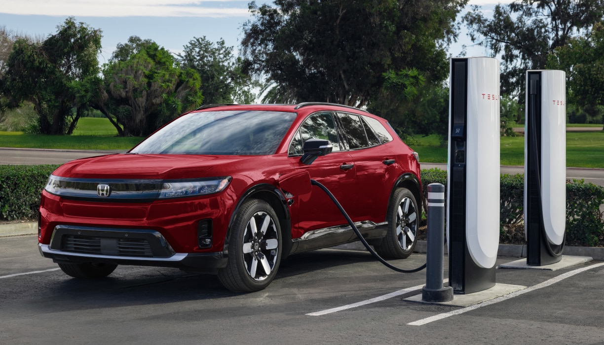 Plan rapproché de trois quarts de bornes de recharge électrique avec des voitures stationnées devant, sous la lumière chaude des rayons solaires.
