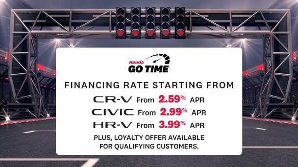 A racetrack inside a stadium with overhead lights and a starting gantry displaying a Honda “Go Time” sign. The sign lists financing rates for CR-V (2.99% APR), Civic (2.99% APR), and HR-V (3.99% APR). Text in the lower left reads “Get on track to your next Honda”, sub-copy reads “Conditions apply. Click Learn more for details” with a “Learn More” button below.