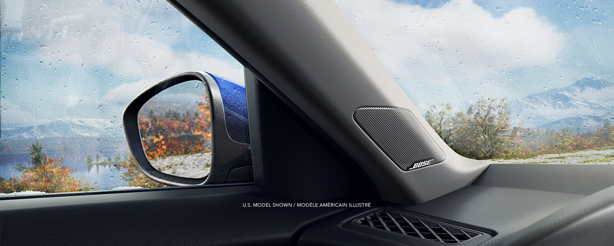 Interior view of door mirror and BOSE® speaker. Out the driver-side window: a mountain range, lake, and trees with orange leaves.