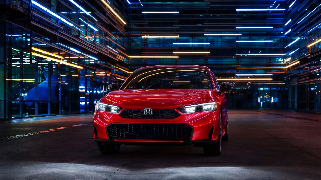 Front view of a parked red Civic Sedan in a dark warehouse-like space.