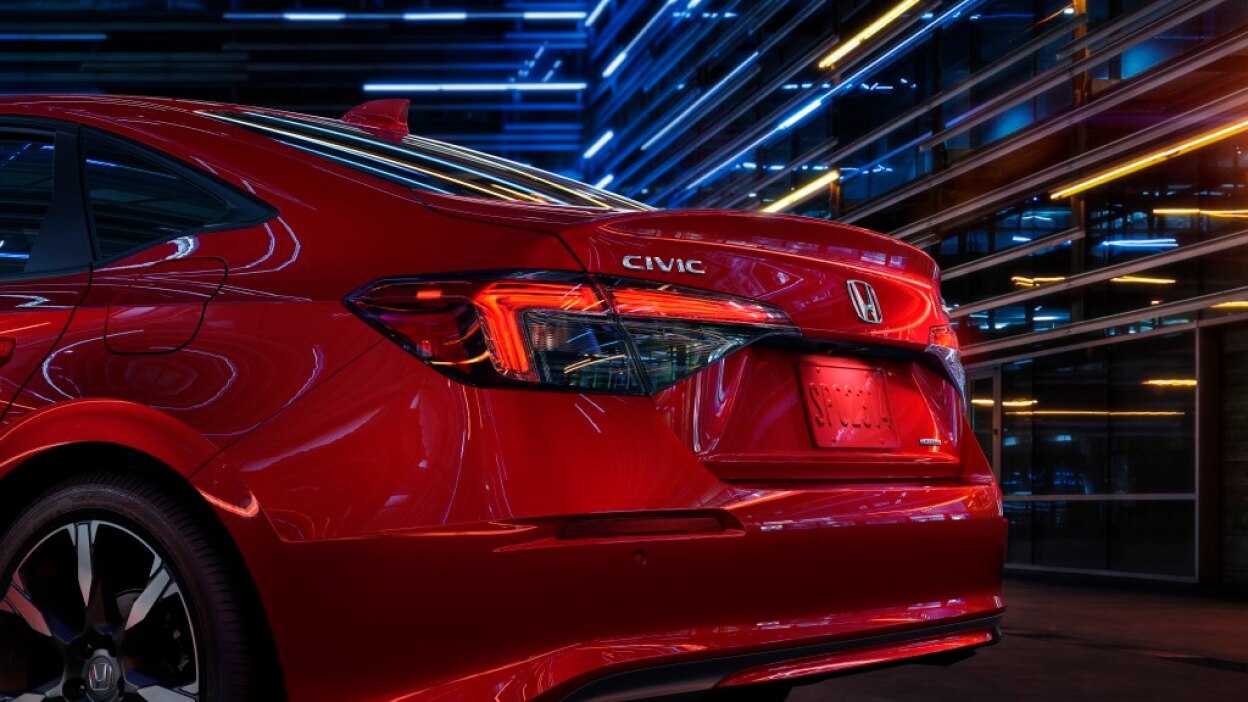 3/4 view closeup of taillight and trunk of a red Civic Sedan in a dark warehouse-like space.