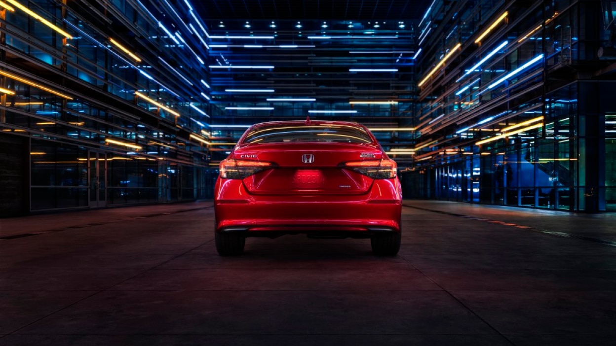 Rear view of a parked red Civic Sedan in a dark warehouse-like space.