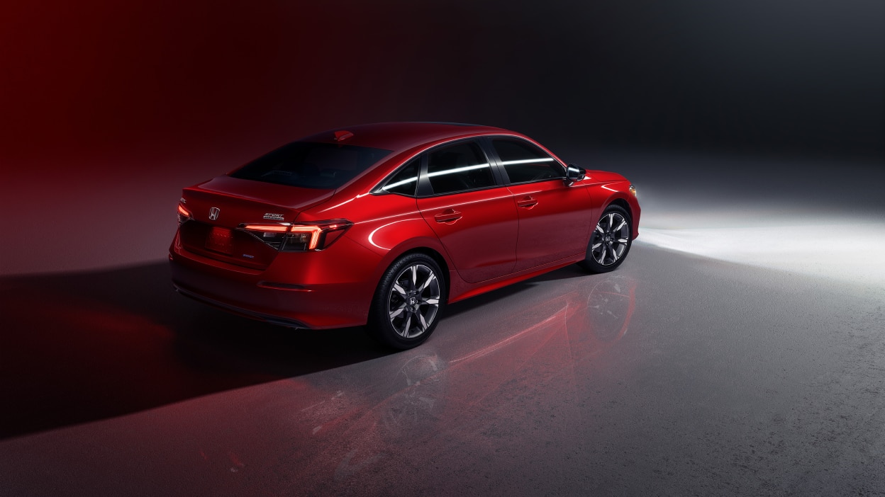 3/4 rear bird’s eye view of a red Civic Sedan parked in a dimly-lit studio-like space.
