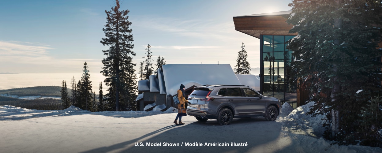 Woman in winter attire opening the tailgate of a grey CR-V outside a snowy ski chalet.