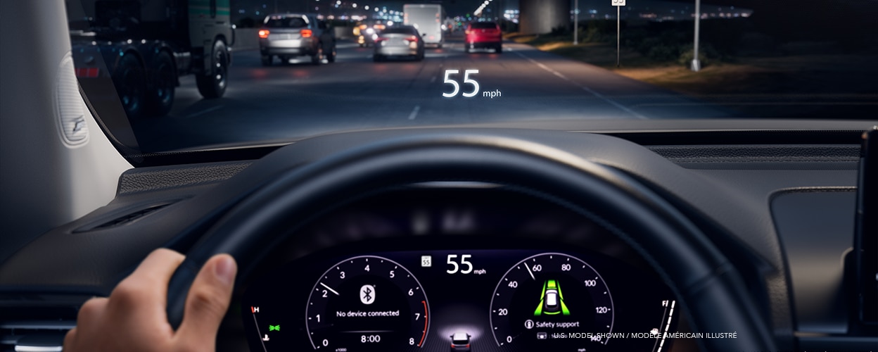 Panoramic wide view of steering wheel, dashboard, and centre console. Out the windshield we see a beautiful forest vista.