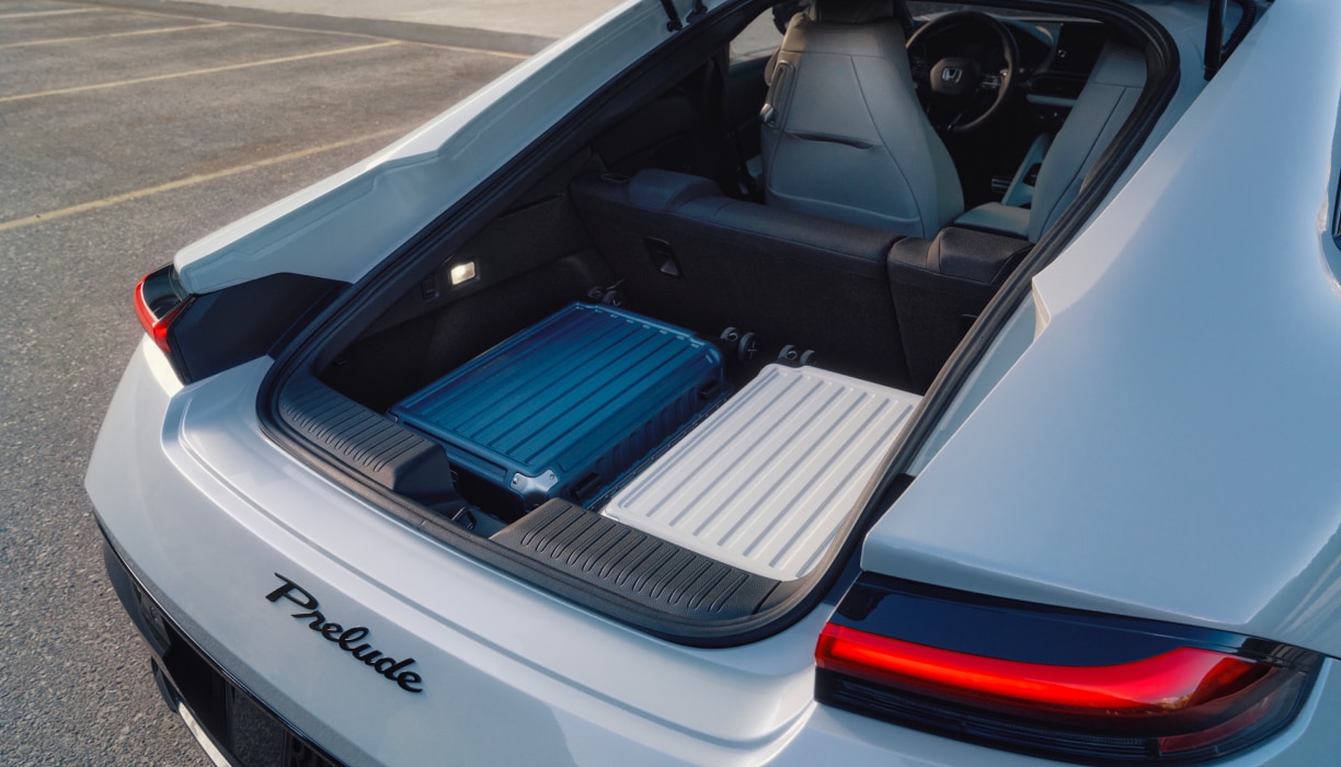 Rear view of the open trunk on a White Prelude with two hardshell suitcases inside.