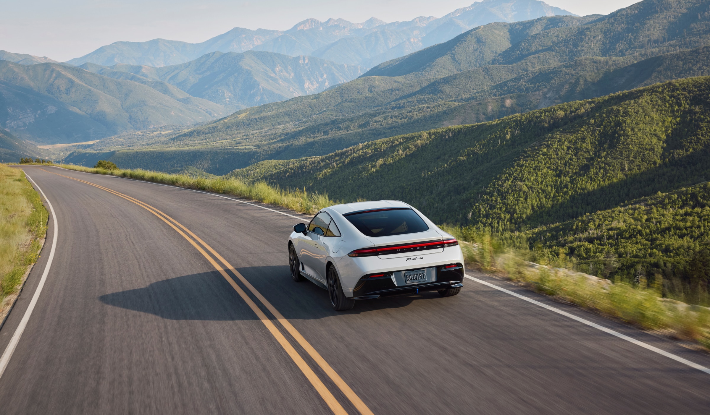 Rear view of white Prelude driving on a highway with mountains in the background.