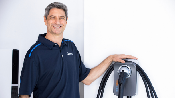 Electrician wearing a Qmerit golf shirt standing next to a wall-mounted ChargePoint+ charging unit.